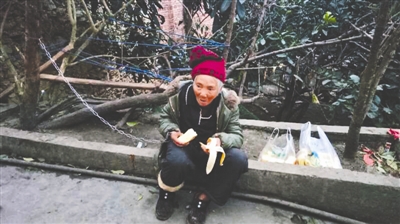 老人坐在屋外的树下，一条铁链将她的右手和树拴在一起